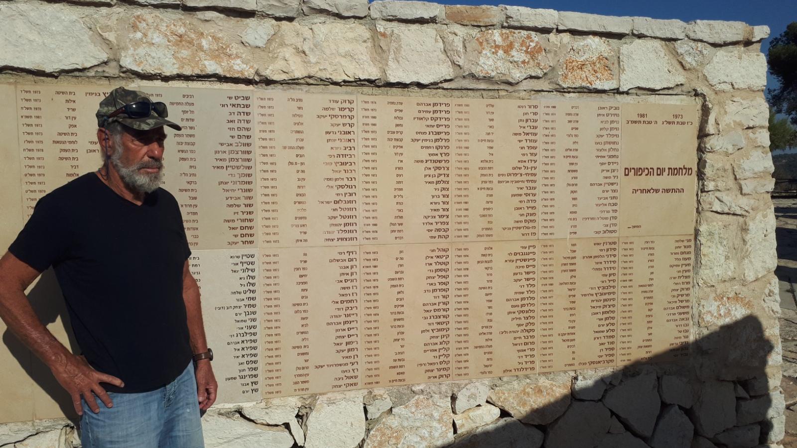 אמנון ישראלי מעין השופט שלחם בחזית הדרום במלחמת יום כיפור ליד הקיר באנדרטה בו חקוקים שמות הנופלים